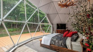 Ein Schlafzimmer mit großem Fenster, einem hölzernen Bett, einem Fernseher und einem Nachttisch.