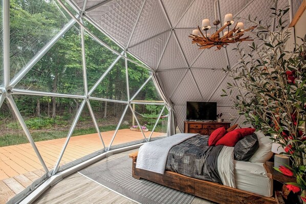 A bedroom with a large window, a wooden bed, a TV, and a nightstand.