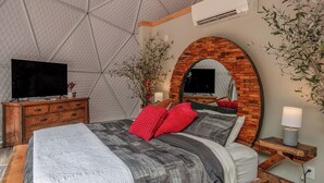 Ein Schlafzimmer mit einem großen Bett, einem Fernseher, einer Holzkommode und einem Spiegel unter einem Ziegelbogen.
