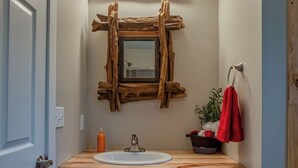 Ein Badezimmer mit einem Holzkosmetikschrank, einem Spiegel mit rustikalem Rahmen und einem roten Handtuch an einem Halter.