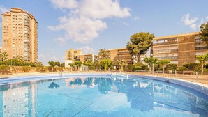 A swimming pool surrounded by buildings with balconies, trees, and a clear sky. - Lovely apartment in Campello (Campello)