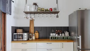 Una cucina con frigorifero in acciaio inossidabile, un piano di lavoro in legno, uno scaffale sospeso con utensili da cucina e un tostapane.
