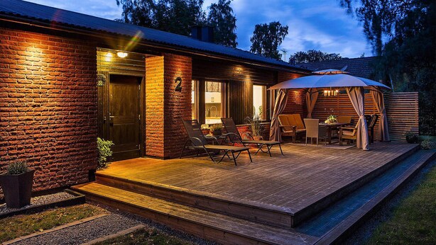 Una casa in mattoni con un patio in legno, arredi da esterno e un portico coperto.