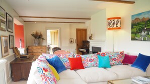A living room with a white sofa adorned with colorful pillows, a glass coffee table, and a fireplace. - Stunning country house (Bix, outside Henley) (Henley)