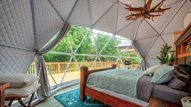 A spacious tented room with a bed, a wooden chair, and a view of the outdoors. - Luxury on the Edge of Traverse City (Williamsburg)