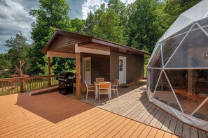 A wooden deck with a covered patio area, a grill, and a seating arrangement. - Luxury on the Edge of Traverse City (Williamsburg)
