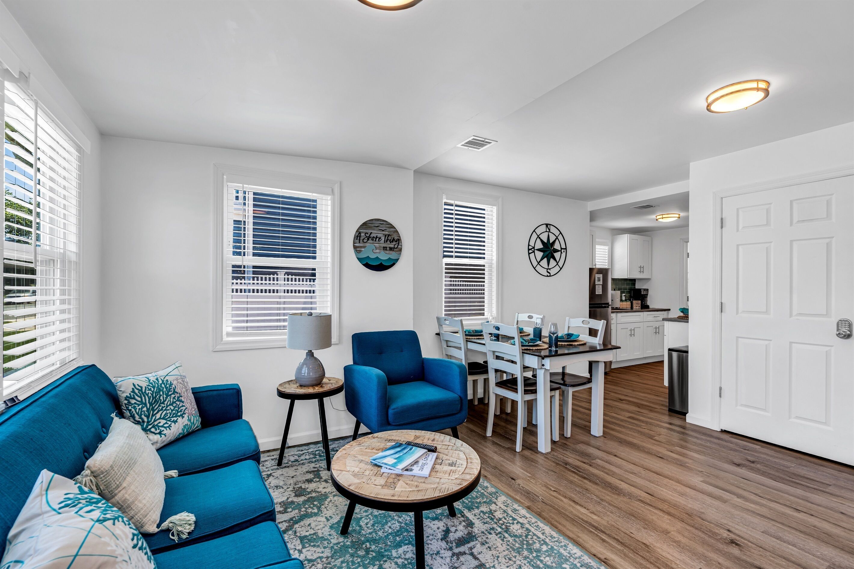 A modern living room with a blue sofa, a round coffee table, and a dining area with white chairs and a table.
