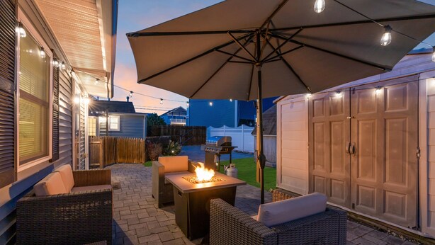 An outdoor patio with wicker furniture, a fire pit, and an umbrella. - THE Unique Belmar Stay | Prime Location. Privacy. 9 Badges. 2 Grills. Fire Pit. (Belmar)