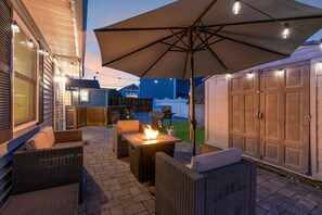 En udendørs terrasse med fletningsmøbler, bålsted og parasol.