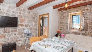 A dining area with a stone wall, wooden beams, a table set for four, and a television mounted on the wall. - Awesome home in Kaprije with WiFi (Kaprije)