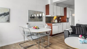 A modern kitchen with white cabinets, a stainless steel range hood, and a dining area with a glass table and chairs. - Beautiful apartment in Fanø with WiFi (Fanø)