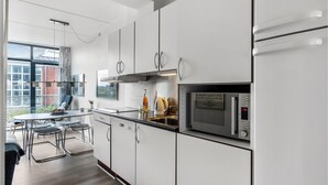A modern kitchen with white cabinets, stainless steel appliances, and a dining area with a glass table and chairs. - Beautiful apartment in Fanø with WiFi (Fanø)