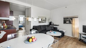 A modern living room with a grey sofa, a round coffee table with fruit, a TV stand, and a dining area with a white table. - Beautiful apartment in Fanø with WiFi (Fanø)