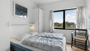 A bedroom with a bed, a chair, a desk, a window with curtains, a wall-mounted lamp, and a painting. - Beautiful apartment in Fanø with WiFi (Fanø)
