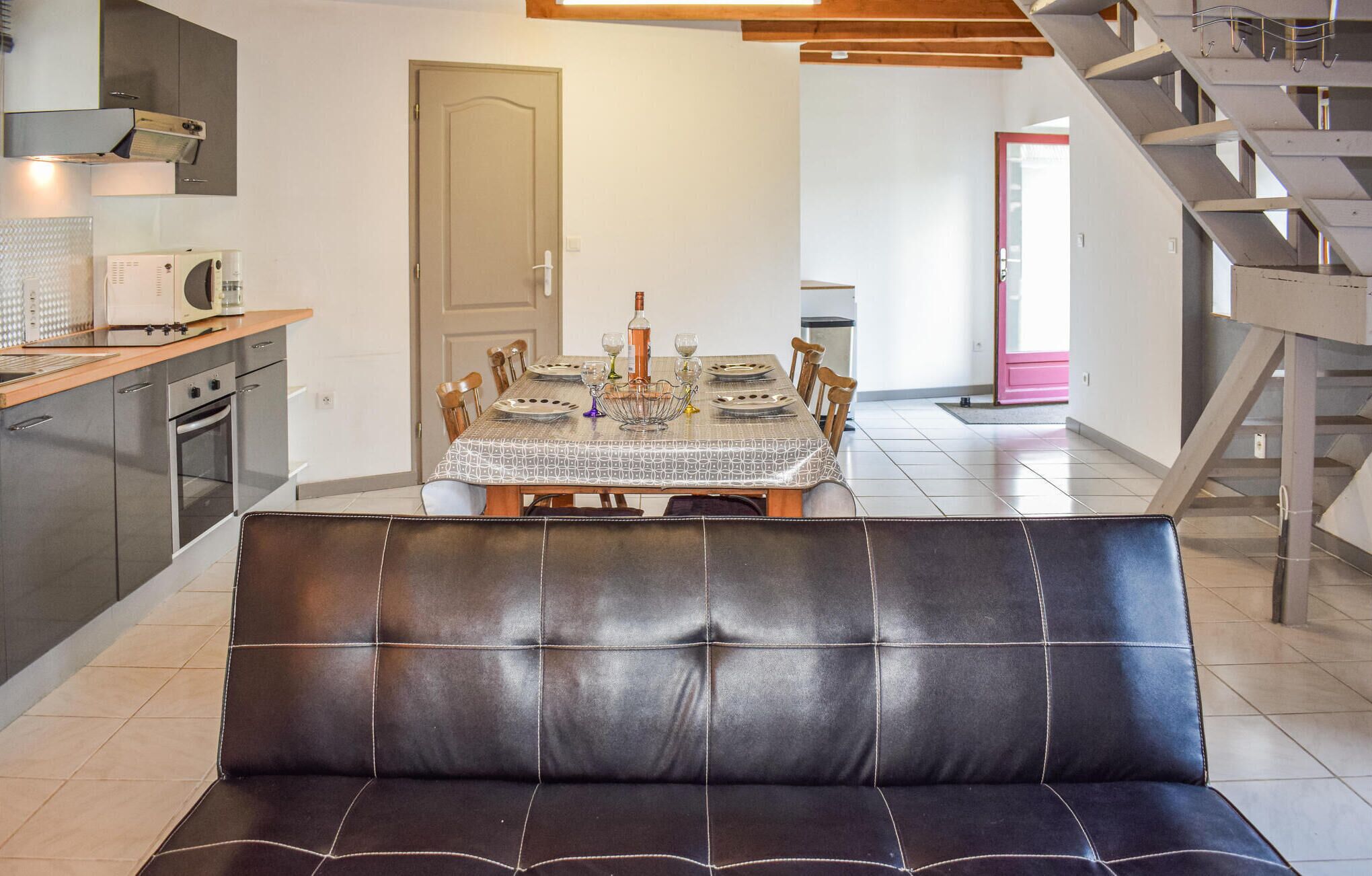 Une cuisine moderne équipée d’appareils électroménagers en acier inoxydable, un coin repas avec une table dressée pour quatre personnes et un escalier.