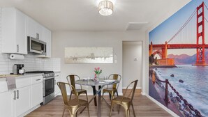Eine moderne Küche mit weißen Schränken, Edelstahlgeräten und einem Essbereich mit einem runden Tisch und vier Stühlen. An der Wand befindet sich ein großes Wandbild der Golden Gate Bridge.