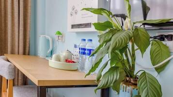 A kitchen area with a wooden table, a potted plant, a kettle, teapot, and bottled water.