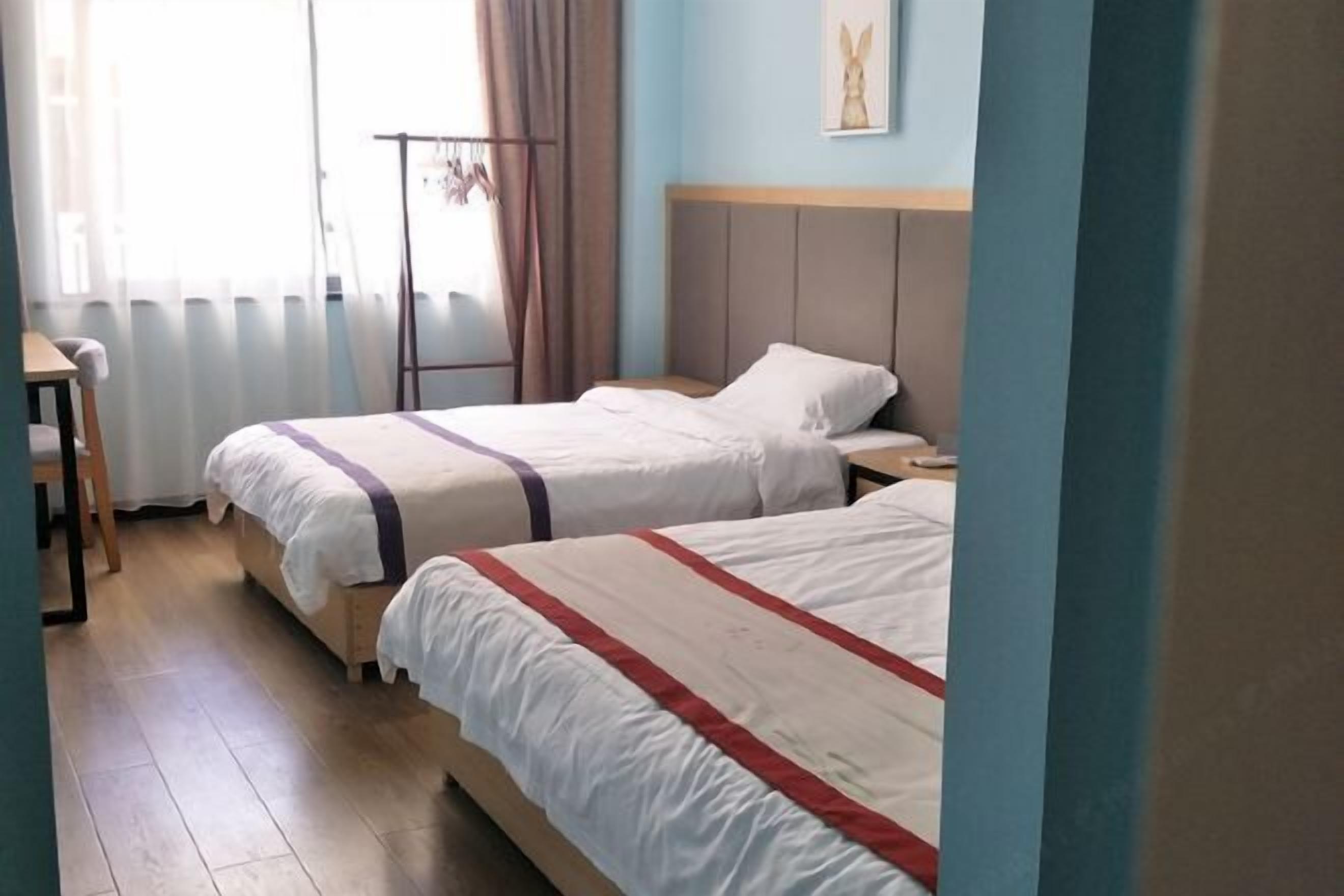 A room with two beds, a wooden floor, a radiator, a window with curtains, and a wall-mounted picture.