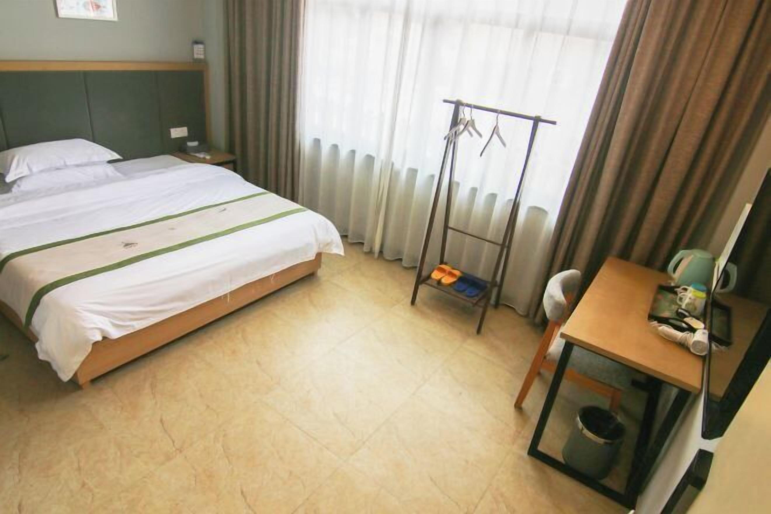 Hotellihuone, jossa on sänky, pieni pöytä, tuoli, patteri ja naulakko.