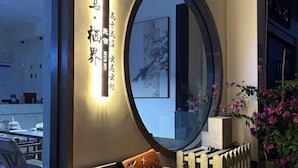 A hotel room with a large round mirror, a bed with orange pillows, a radiator, and a wall with framed artwork. - Migratory Haven · Xishan Hidden Inn (Wuyishan)