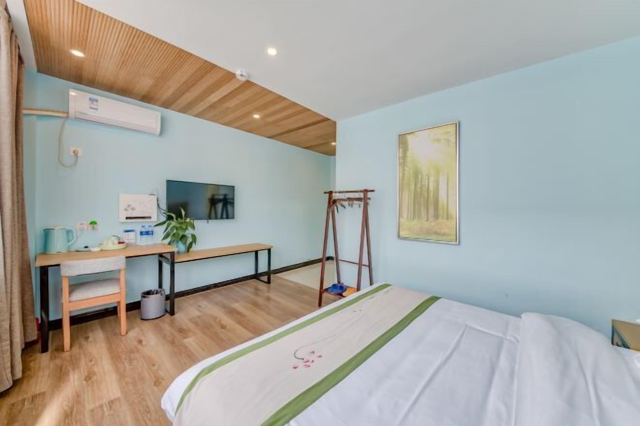 A bedroom with a bed, a desk, a chair, a wooden ceiling, and a painting on the wall.