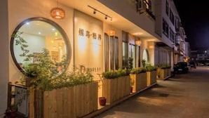 A hotel facade with illuminated signage, a wooden fence with potted plants, and a street view at night. - Migratory Haven · Xishan Hidden Inn (Wuyishan)