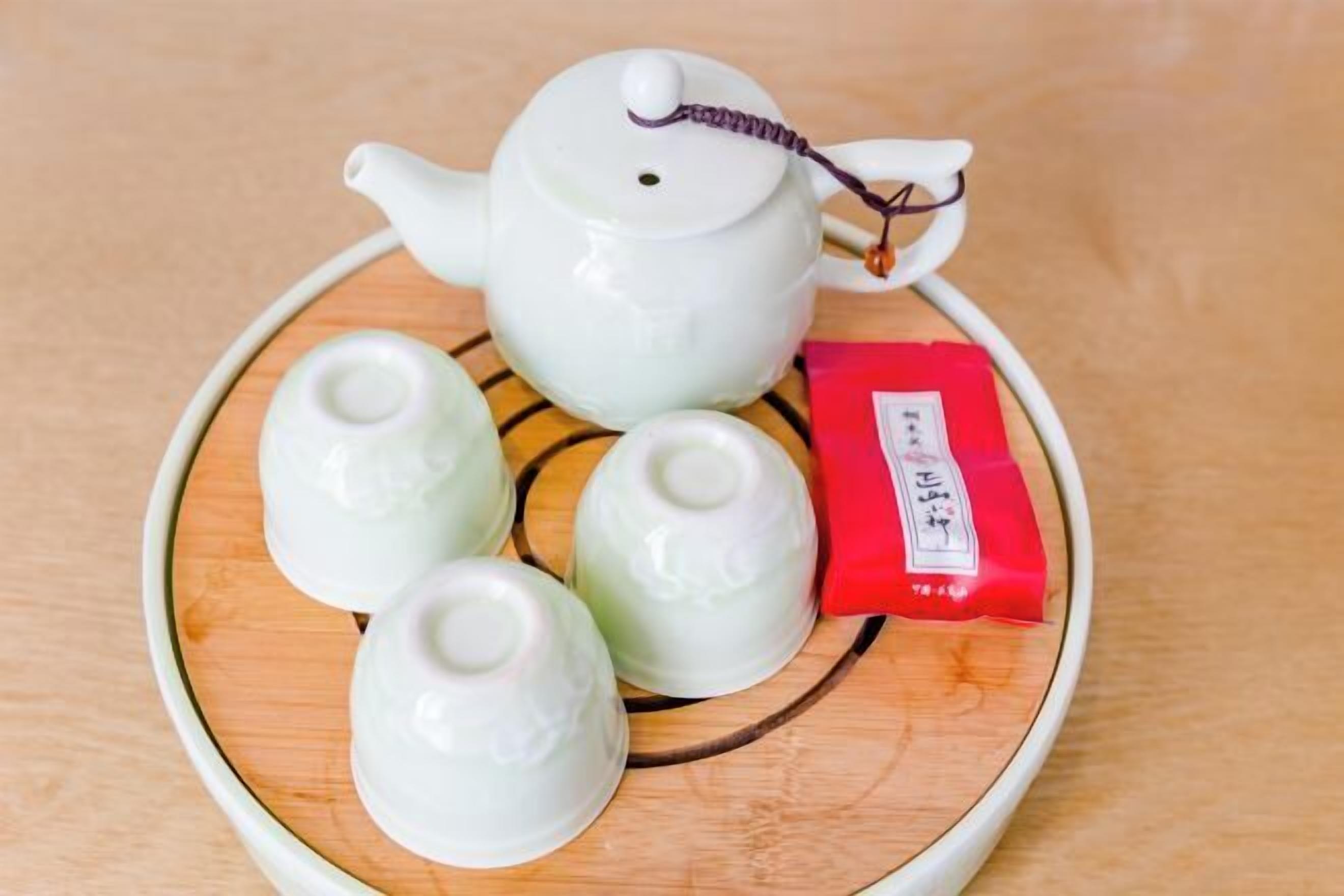 A white teapot with a lid and a tea bag on a tray.