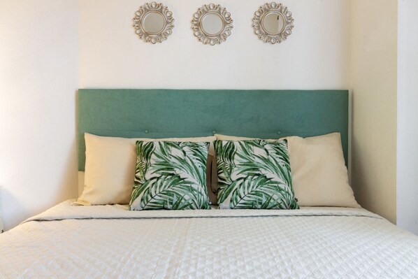 Un lit avec une tête de lit verte, deux miroirs décoratifs et un coussin à motifs.
