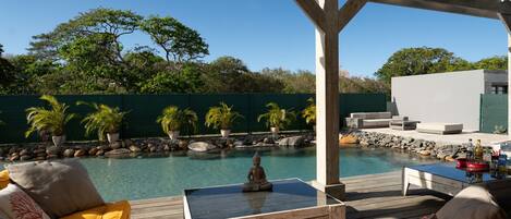 A wooden deck with a pool, outdoor furniture, and a green fence.