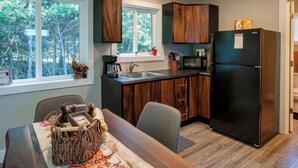 A modern kitchen with dark wood cabinets, a black refrigerator, and a window overlooking a forest. - Luxury on the Edge of Traverse City - 6 (Williamsburg)
