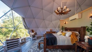 A spacious bedroom with a large bed, a wooden bench, a small table, and a hanging light fixture. - Luxury on the Edge of Traverse City - 6 (Williamsburg)