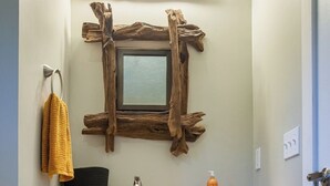A rustic bathroom with a wooden vanity, a mirror with a natural frame, and a yellow towel hanging on the wall. - Luxury on the Edge of Traverse City - 6 (Williamsburg)