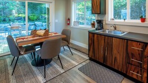 A modern kitchen with a wooden cabinet, a sink, and a dining area with a table and chairs. - Luxury on the Edge of Traverse City - 6 (Williamsburg)