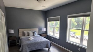 A bedroom with a bed, nightstands, and two windows.