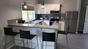 A modern kitchen with a central island, bar stools, stainless steel appliances, and pendant lighting.