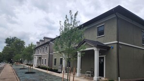 A row of modern, two-story townhouses with a covered front porch and a landscaped front yard.