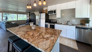A modern kitchen with a granite island, white cabinets, and a built-in microwave. - Osito Cabin - Pet Friendly | Hot Tub | Fire Pit | Ms. Pac Man | Telescope (Angel Fire)