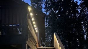 A wooden staircase leading to a deck with railings and lights. - Osito Cabin - Pet Friendly | Hot Tub | Fire Pit | Ms. Pac Man | Telescope (Angel Fire)