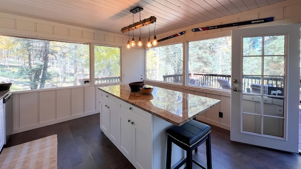 A kitchen with a large island, white cabinetry, and a view of the outdoors through large windows. - Osito Cabin - Pet Friendly | Hot Tub | Fire Pit | Ms. Pac Man | Telescope (Angel Fire)