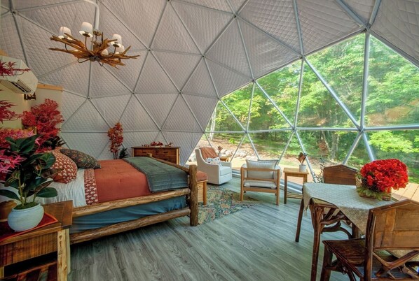 A geodesic dome room with a bed, seating area, and a dining table.