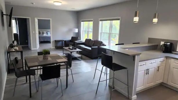 Una cocina moderna con una isla central, zona de comedor con sillas y espacio de sala de estar con sofá y mesa de centro.