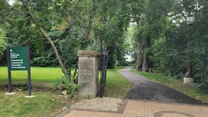 Un sendero pavimentado que atraviesa un parque con un cartel verde que enumera atracciones cercanas.
