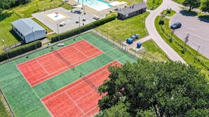 Oversigtsbillede af en sportskompolex med tennisbane, swimmingpool og en mindre bygning.