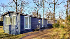 En etagers, mørk campingvogn med en belagt indkørsel og et gyngestativ i haven.