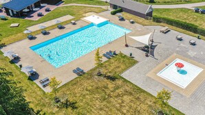 En stor, rektangulær swimmingpool med en skyggefuld soldæk, omgivet af liggestole og parasoller.