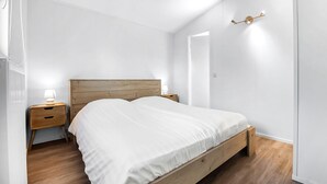 Et minimalistisk soveværelse med en træseng, to sengeborde med lamper og et enkelt vægmonteret lys.