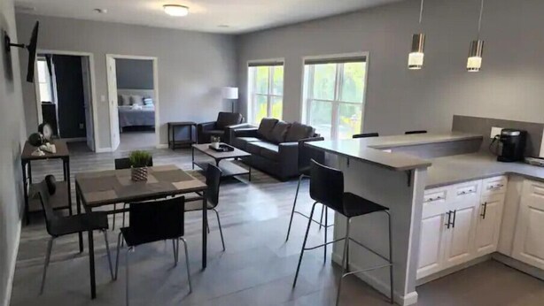 A modern kitchen with a central island, dining area with chairs, and a living space with a sofa and coffee table.