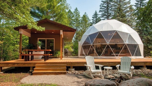 Een houten hut met een terras en een geodetische koepelconstructie.