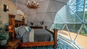 Een slaapkamer met een geometrisch plafond, een houten bed, een nachtkastje en uitzicht op het omliggende landschap.