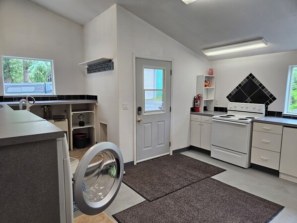 A compact kitchen with a washing machine, a stove, and a small window. - Valdez Home - Fishing and Mountain Adventures (Valdez)